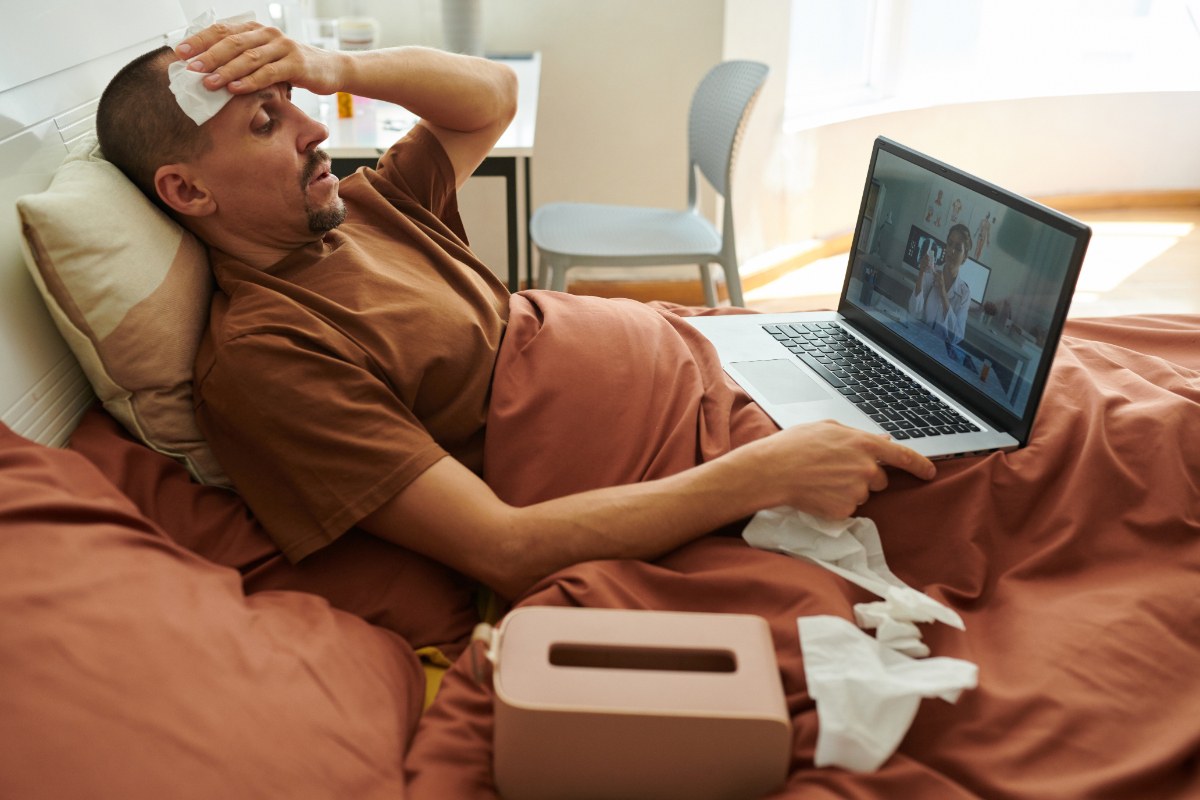 Un homme allongé sur le lit avec son ordinateur et des mouchoirs