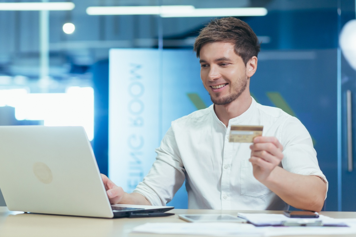 Un jeune homme assis dans un bureau avec une carte de crédit devant son ordinateur