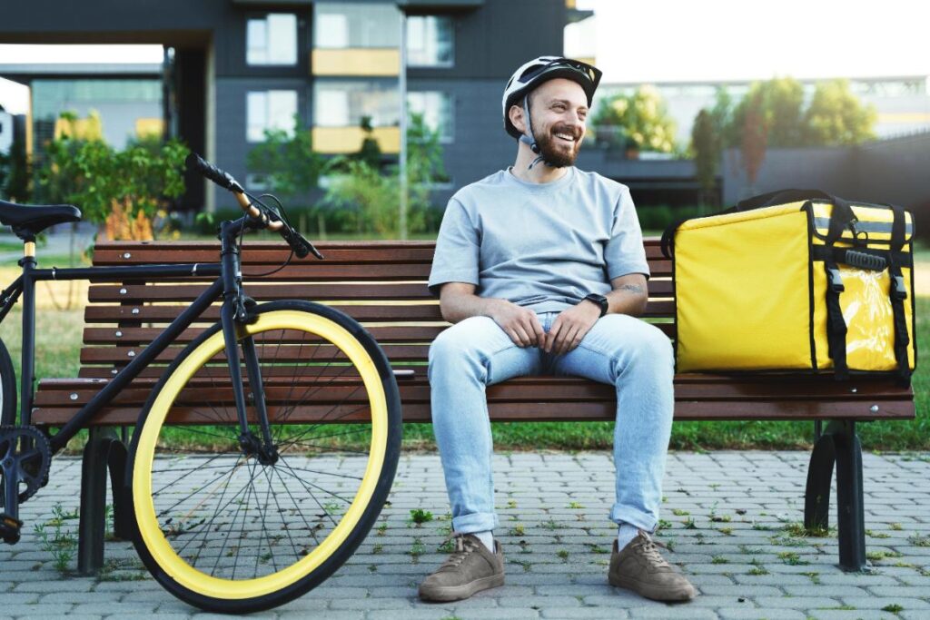 Un livreur assis sur un banc avec un sac isotherme et un vélo