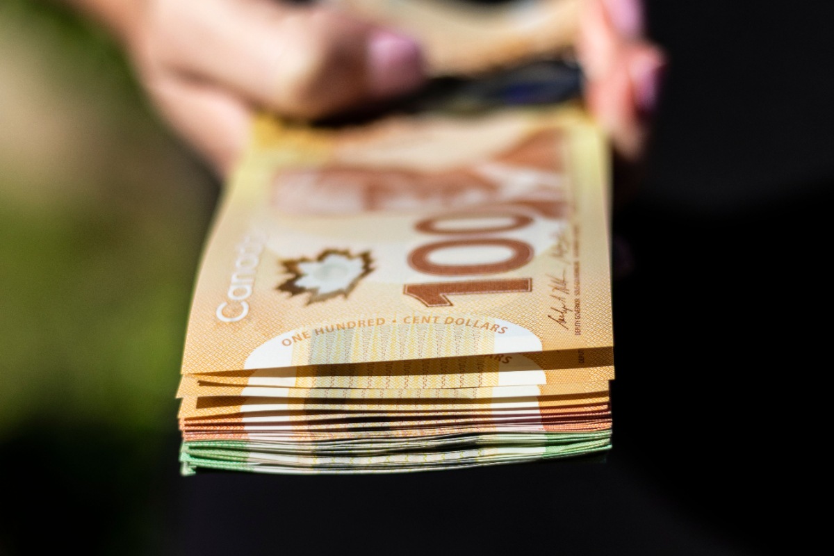 Une main tenant un billet de cent dollars canadien