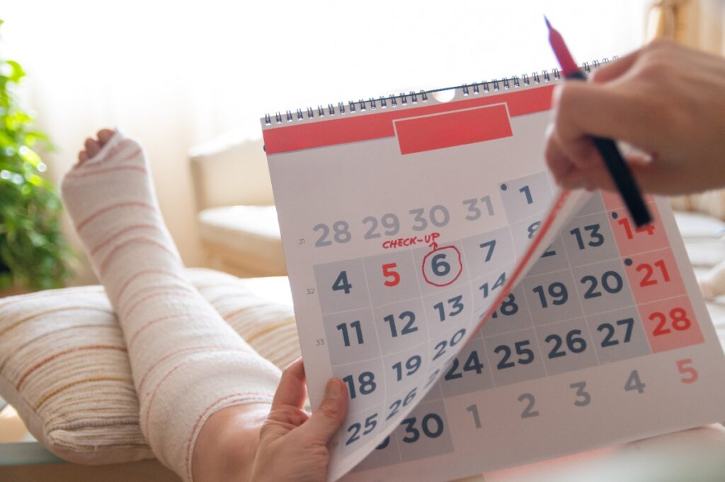 Une personne ayant un plâtre au jambe et tenant un calendrier er un stylo