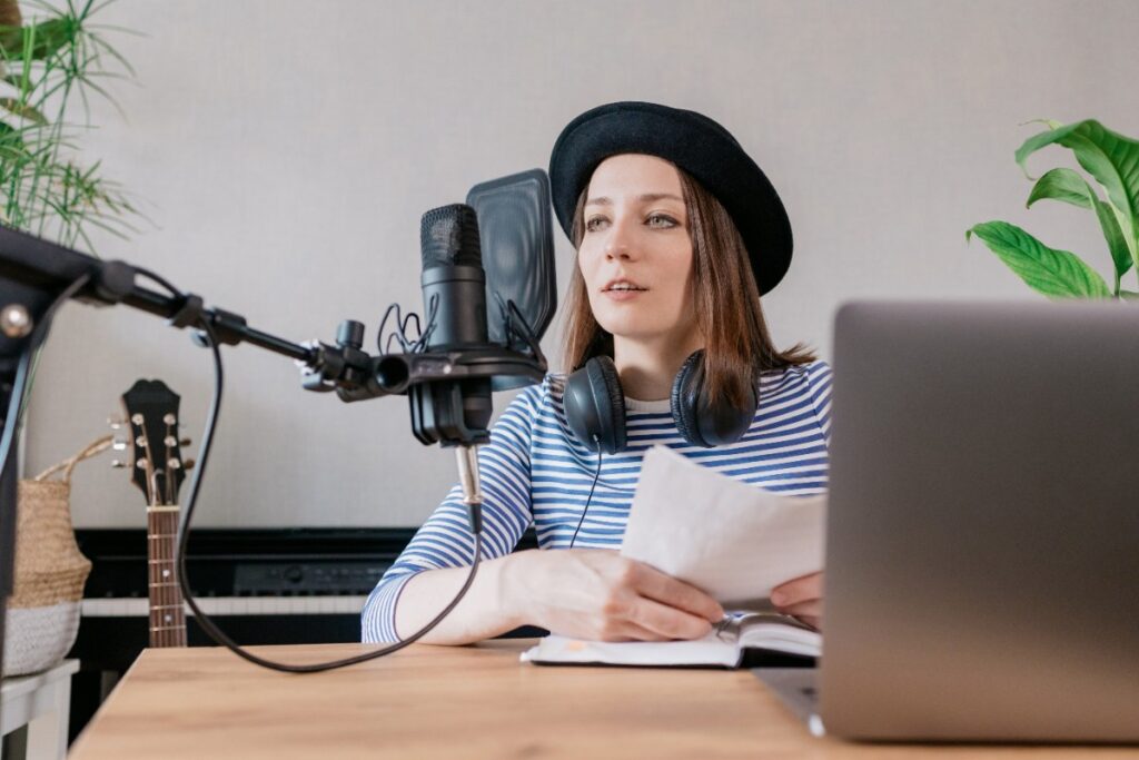 Une femme portant un chapeau et une lunette, en enregistrant un podcast dans un studio