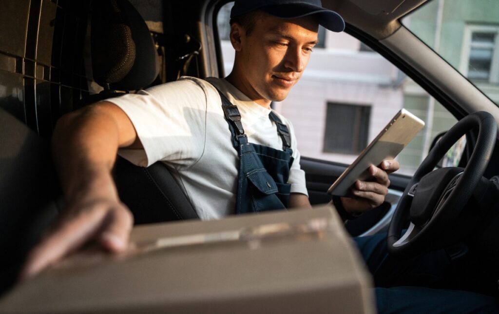 Un livreur qui regarde une tablette et tenant un colis dans une voiture