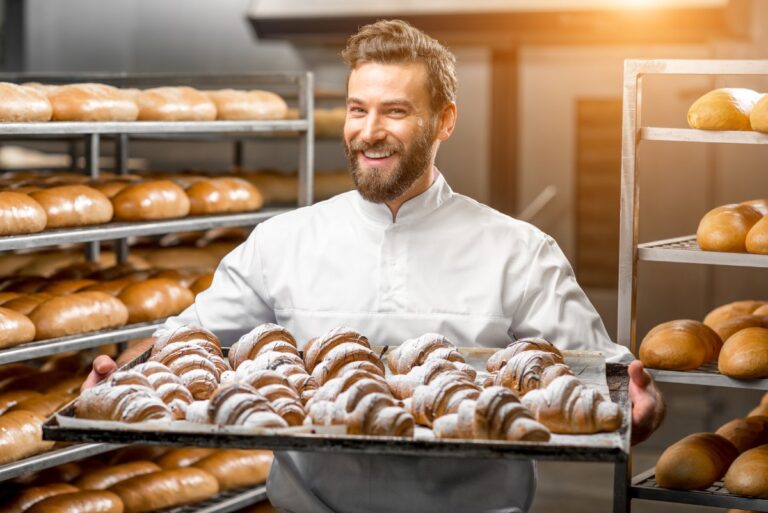 Un boulanger souriant tenant un plateau rempli de croissant