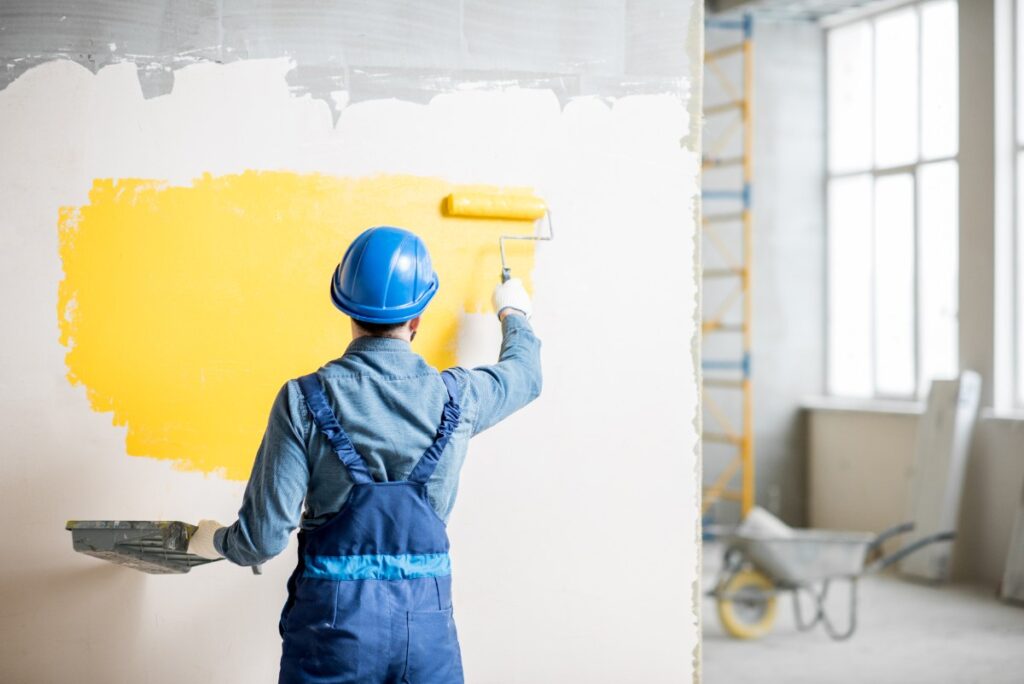 Un ouvrier peignant le m:ur avec une peinture jaune 